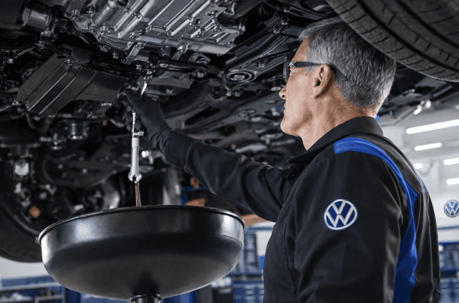 Volkswagen technician performing oil change under a vehicle during routine maintenance service