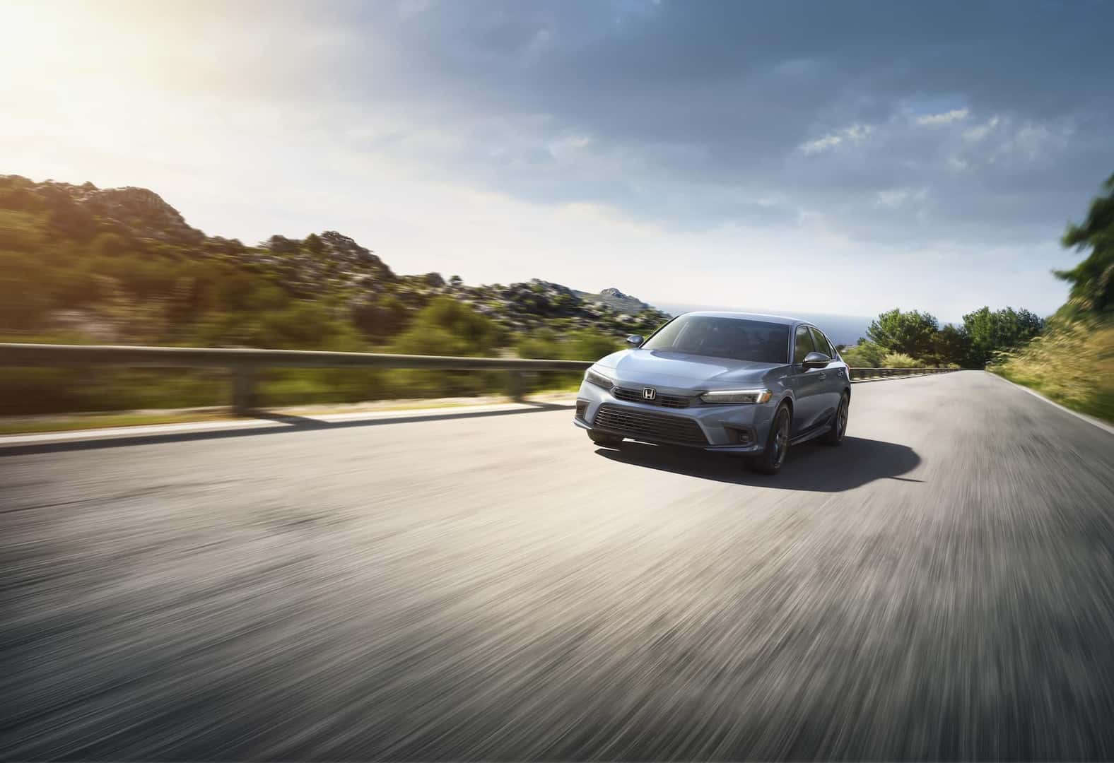2023 Honda Civic driving on a highway with woods in the background