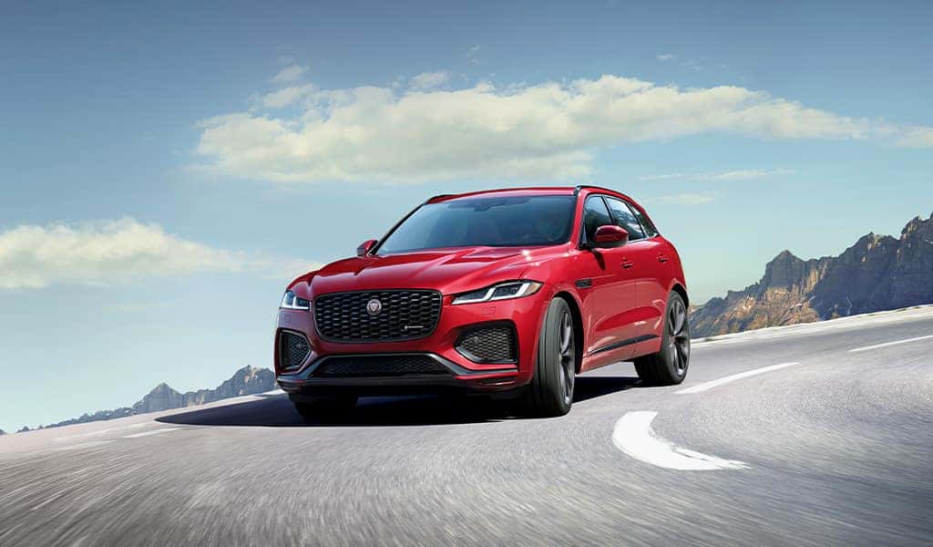 A red 2023 Jaguar F-PACE vehicle driving on the road and making a sharp turn with mountains in the background.