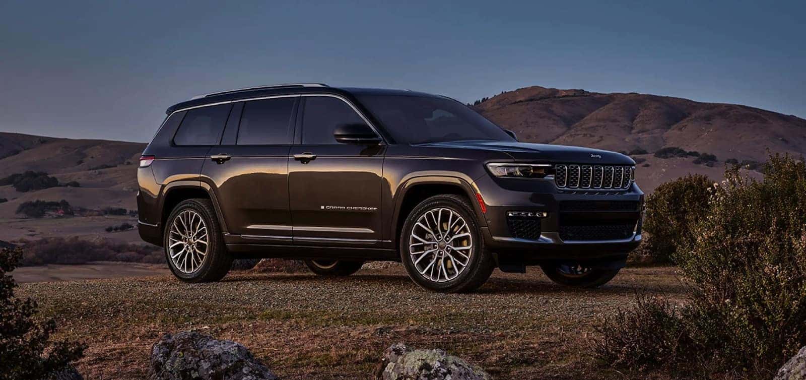 Black 2023 Grand Cherokee L parked on a deserted road with mountains in the background.