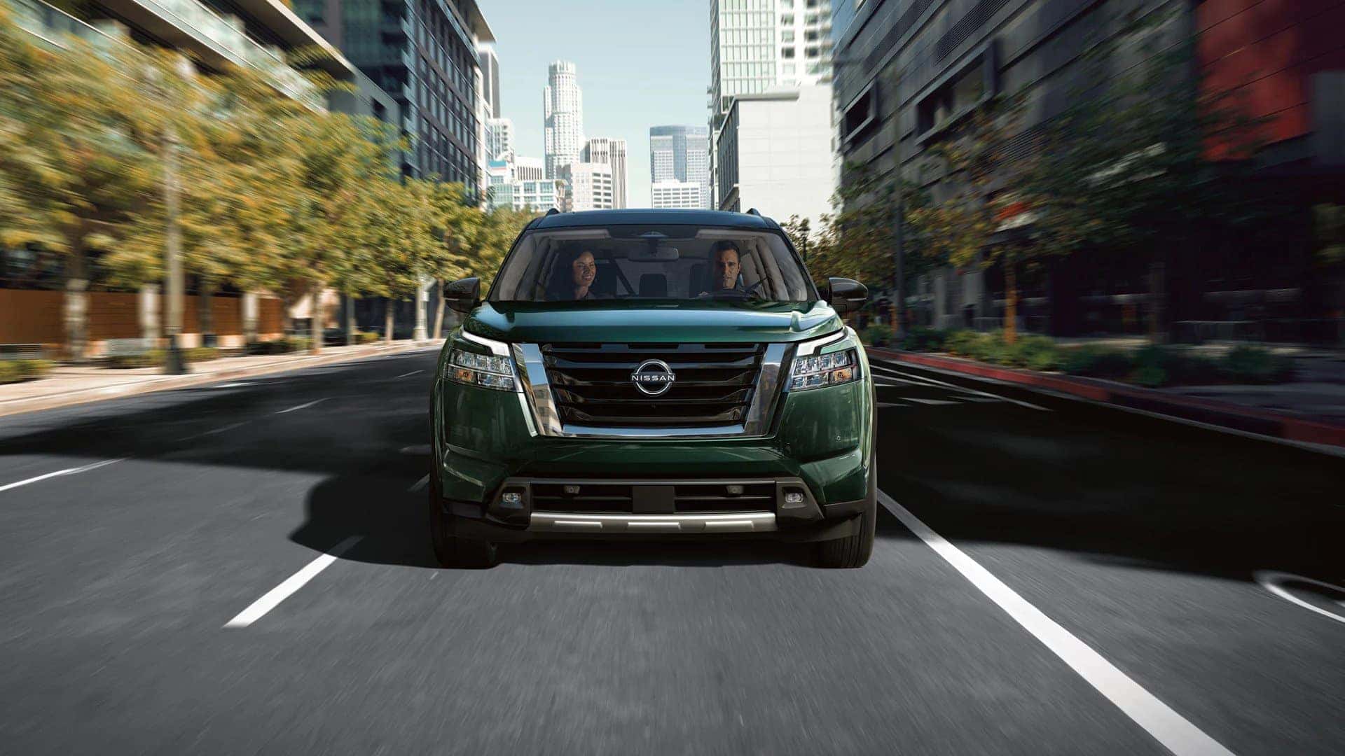 Man and woman driving a green 2022 Nissan Pathfinder and a city street