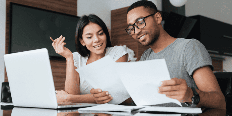 Couple reviewing documents together at a coffee table with a laptop nearby