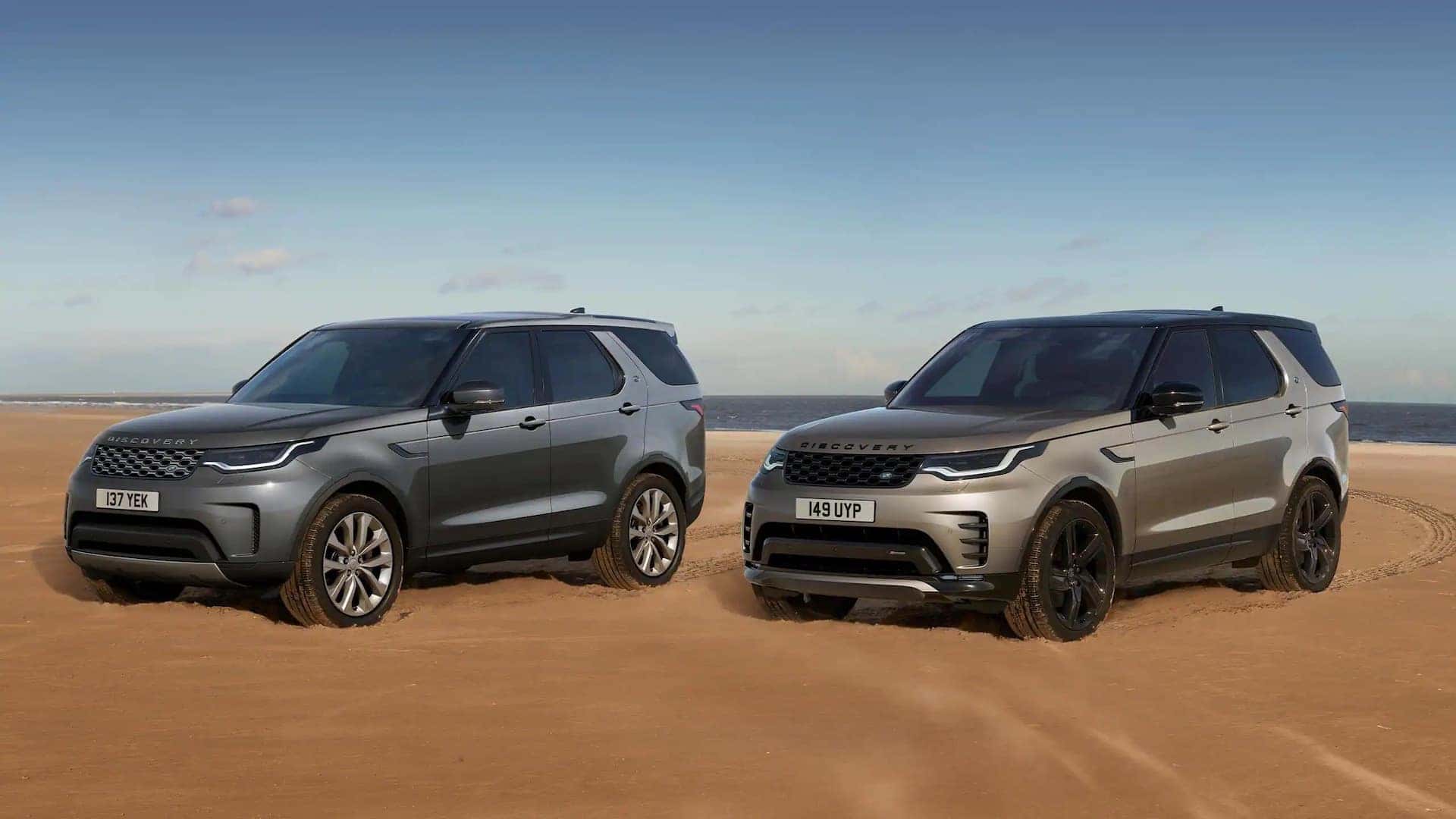 Two Land Rover Discovery Sports with the color gray on the left and the color tan on the right, parked in a desert. 