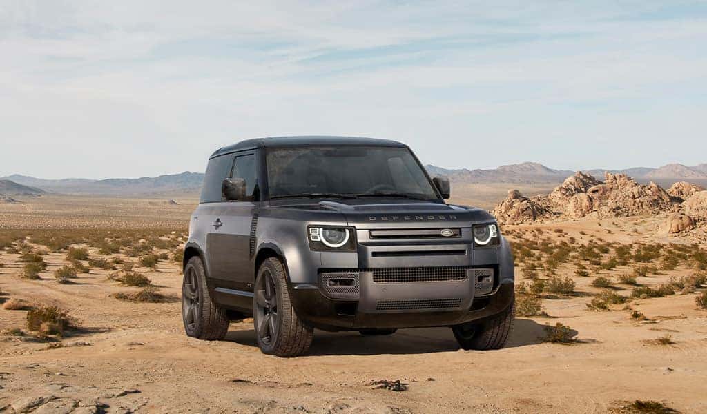  A dark grey 2023 Land Rover Defender parked in a desert with mountains in the background. 