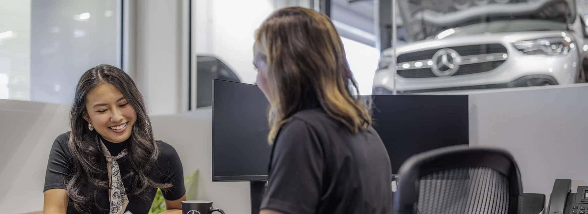 woman looking down and smiling across a desk from an employee at a dealership
