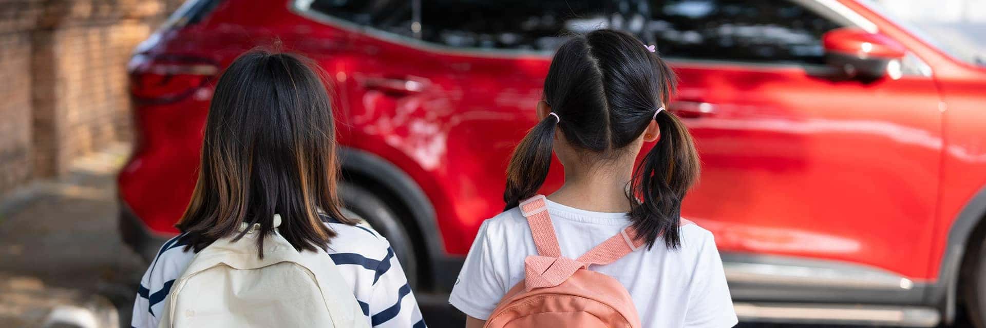 two kids with backpacks walking towards red car