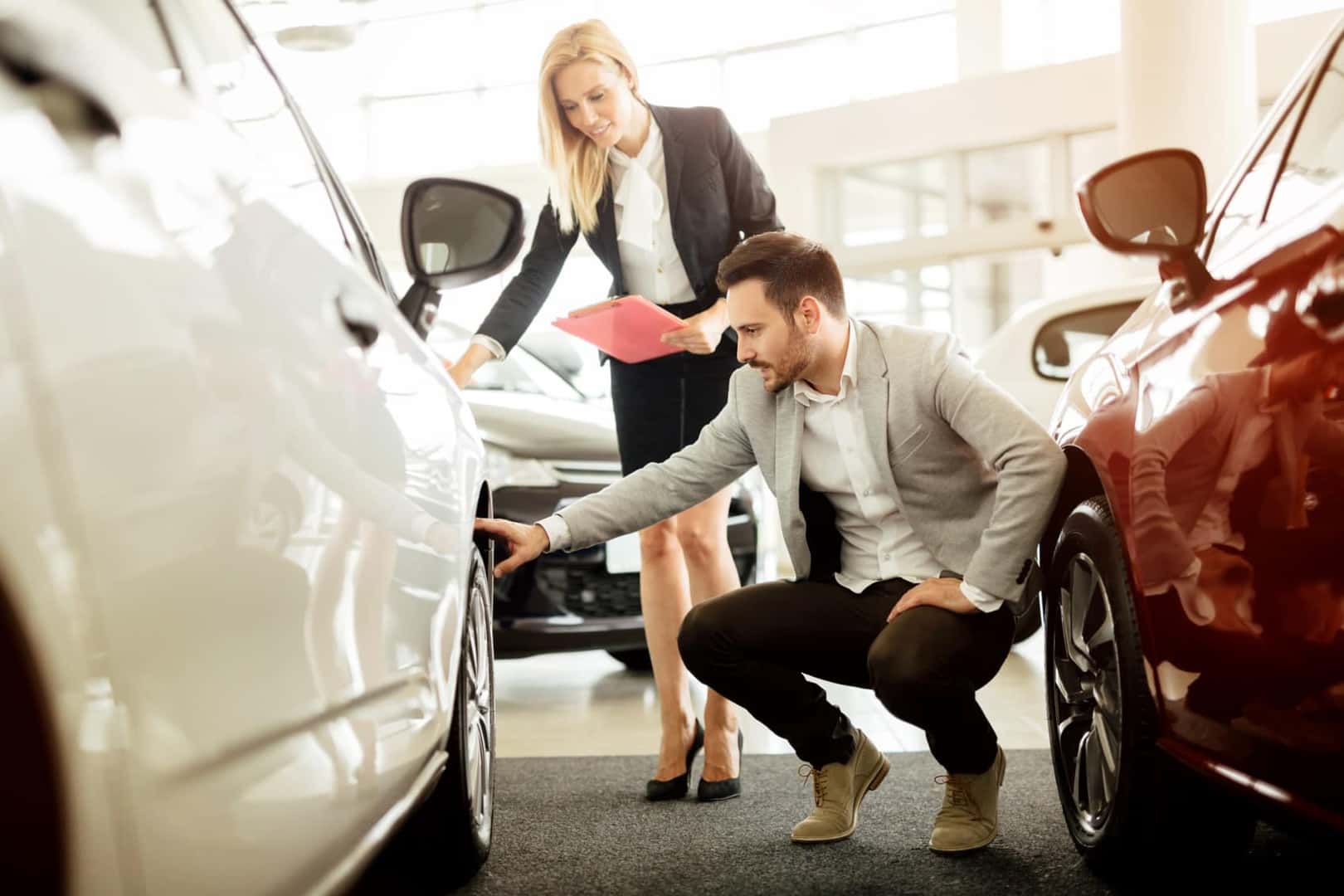 Woman and man closely inspecting new car in dealership showroom