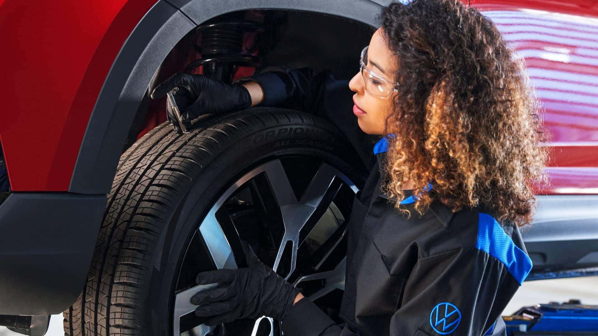 female VW service tech doing a tire inspection