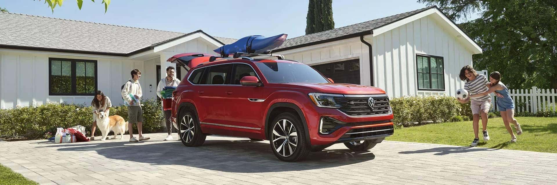 Red 2025 VW Atlas in front of a white house with a family packing for a trip with kids running around. 