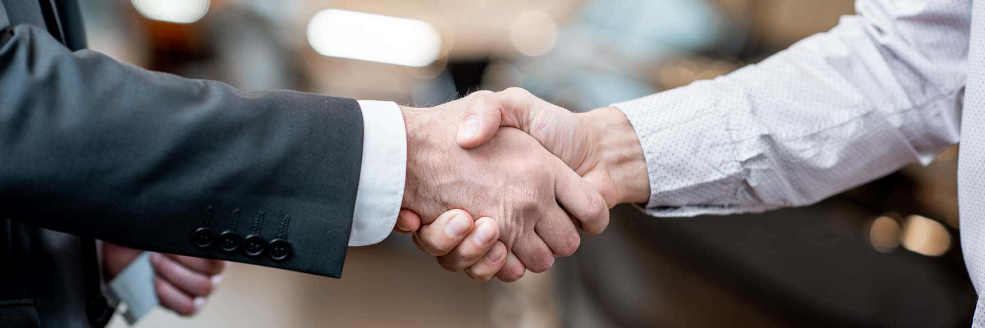 two people shaking hands in front of vehicles at a dealership