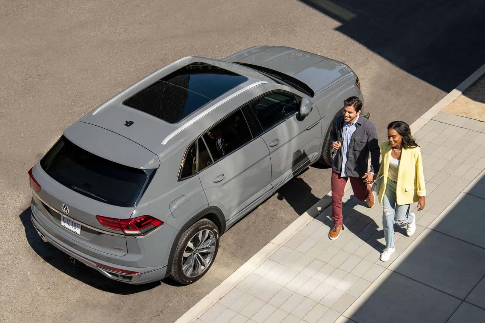 couple walking next to gray atlas cross sport parked on street