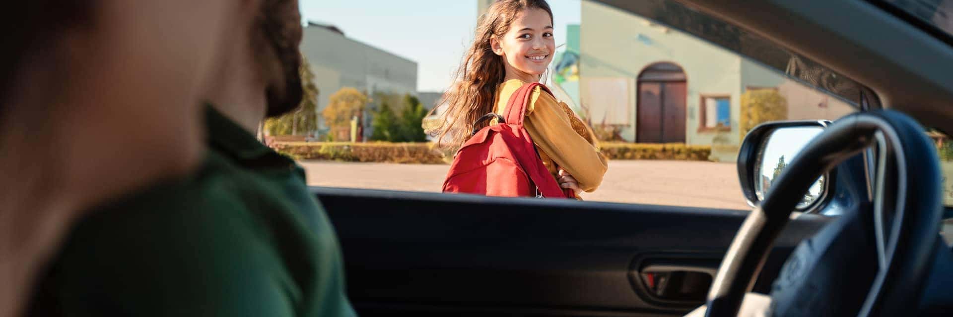parents watching child walk into school from vehicle