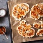 roasted cauliflower steaks with spice on baking tray. plant based meat substitute