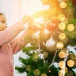 A young Black girl putting ornaments and lights on a Christmas tree.