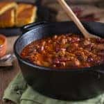 a cast iron bowl of chili with bread blurred in the background
