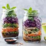 Healthy asian salad with noodles, vegetables, chicken and tofu in glass jars. Grey background