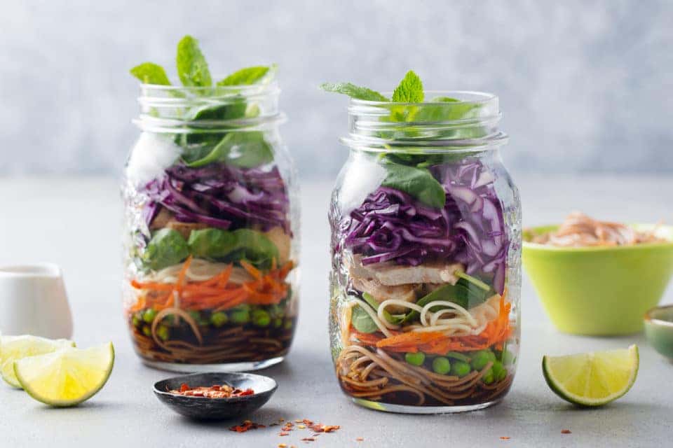 Healthy asian salad with noodles, vegetables, chicken and tofu in glass jars. Grey background