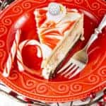 A slice of candy cane cheesecake on a festive red plate with fork and a candy cane garnish.