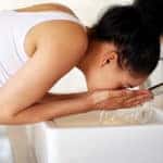 Young woman washing her face at a bathroom sink