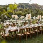 A wedding table set up in the woods. Boho vibe. Greenery, glass, pampas grass, white linens.