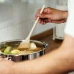 Man stirs soup cooking on the stove.