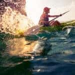 kayaker splashing in choppy water with sun glowing in the spray