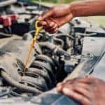 hands under hood of car checking oil