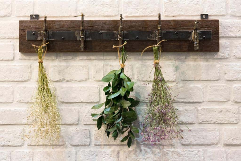 Wooden vintage style Hanger / Hooks on white brick wall decorated with dried bouquets in a country style home.