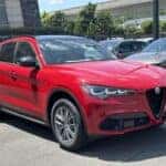 A red 2024 Alfa Romeo Stelvio Sprint SUV parked in a spacious parking lot, showcasing its sleek design and vibrant color.