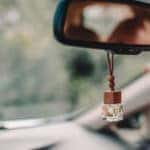 Car air perfume freshener inside the car with blurred green background. Little glass bottle with wooden lid and yellow aromatic liquid automobile freshener on car mirror.