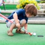 Little boy playing mini golf.