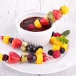 Fruit kabobs on a white plate with a cup of chocolate dipping sauce