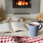Book and cup of tea near burning fireplace.