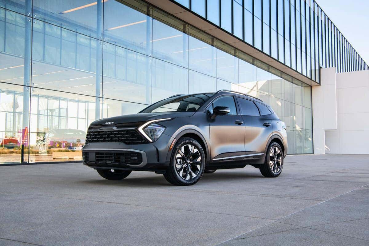 A 2025 KIA Sportage PHEV parked in front of a large modern building, showcasing its sleek design and urban setting.