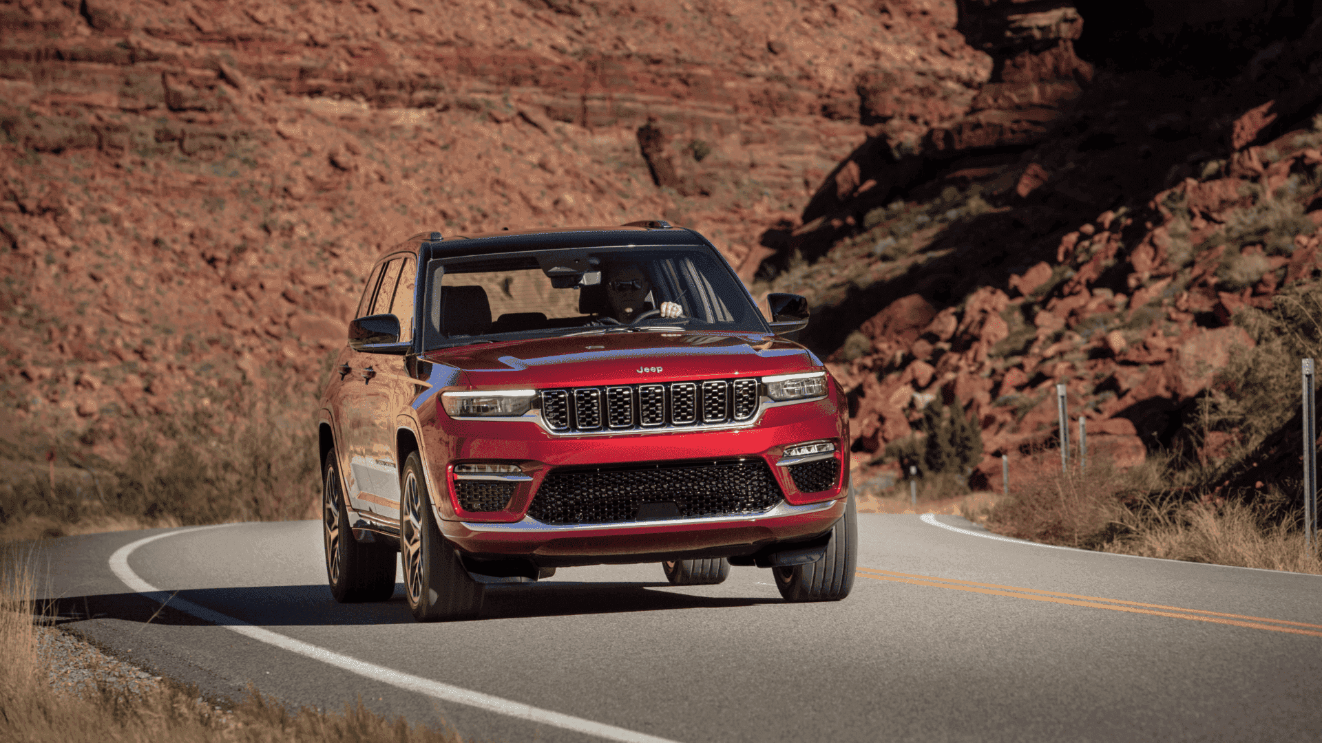 2025 Jeep® Grand Cherokee in red rounding a canyon curve with rock formations in view