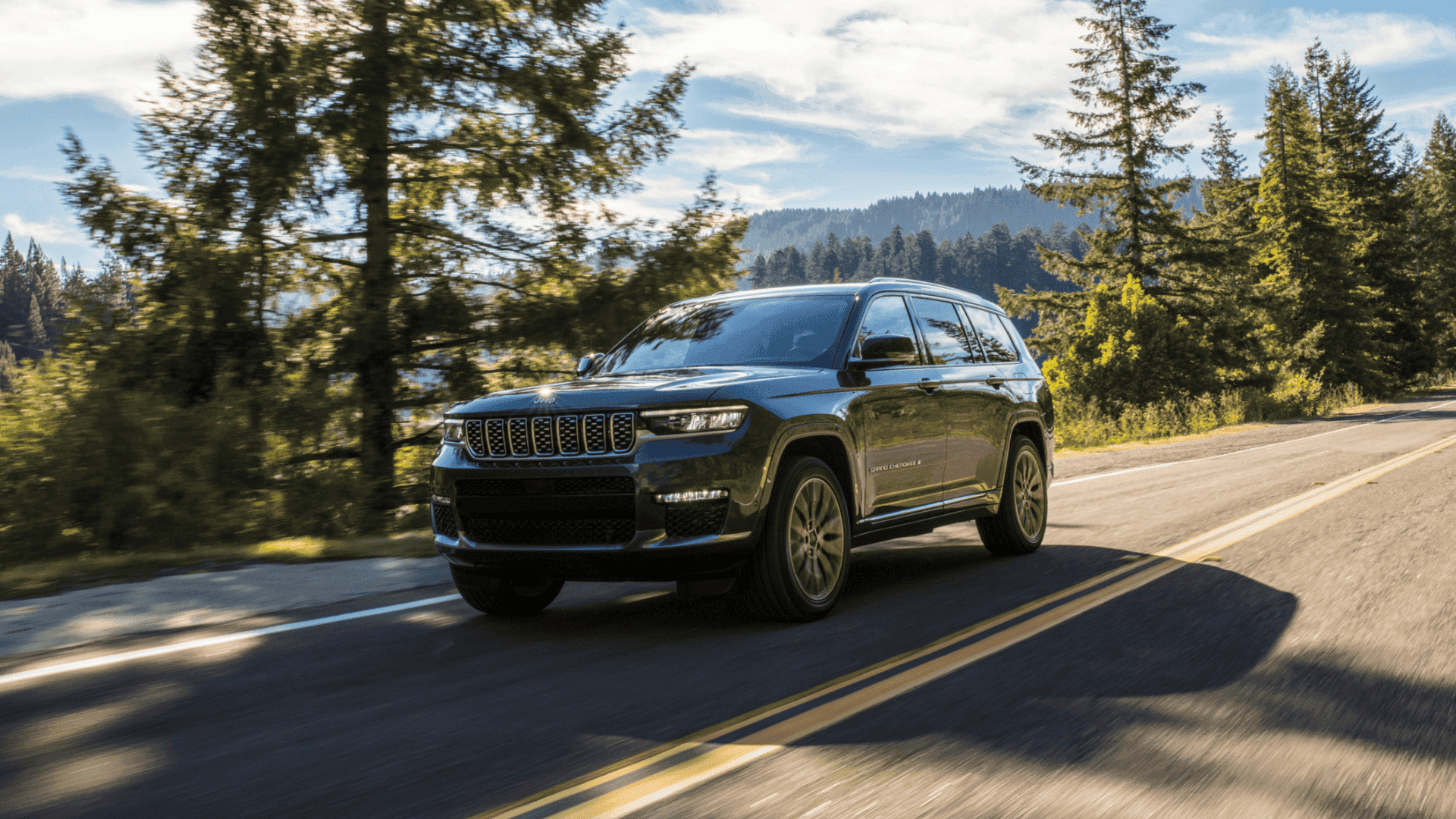 2025 Jeep® Grand Cherokee L driving on a forest highway with tall trees on both sides