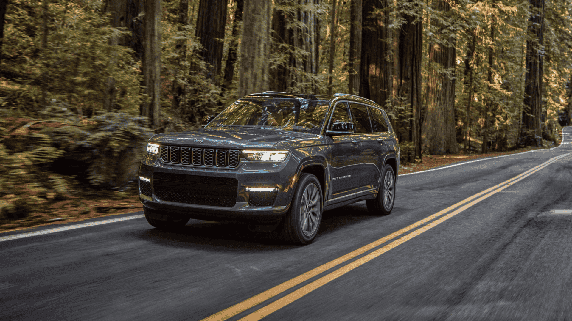 2025 Grand Cherokee L driving on a forest road with motion blur on the wheels and trees