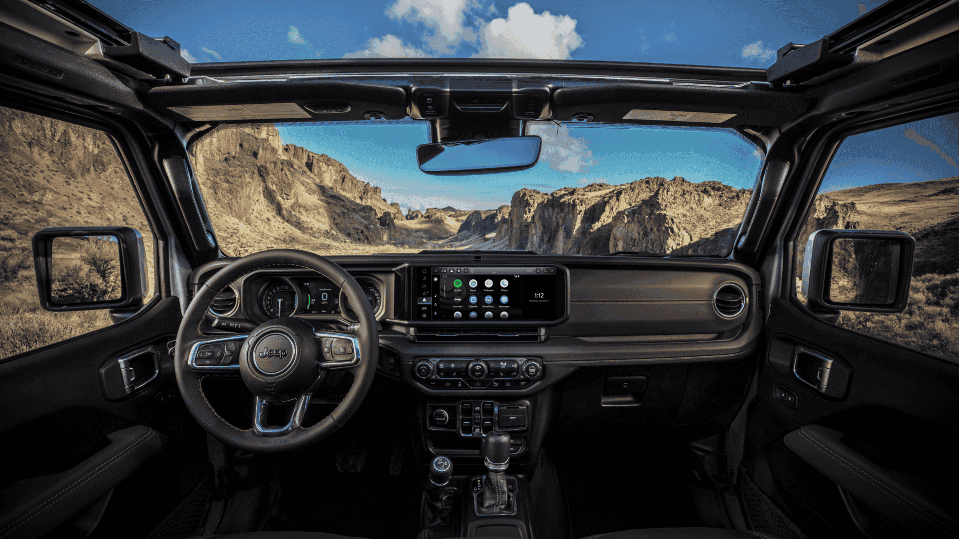 2025 Jeep Wrangler 4xe cabin with open roof, touchscreen, and rugged mountain view