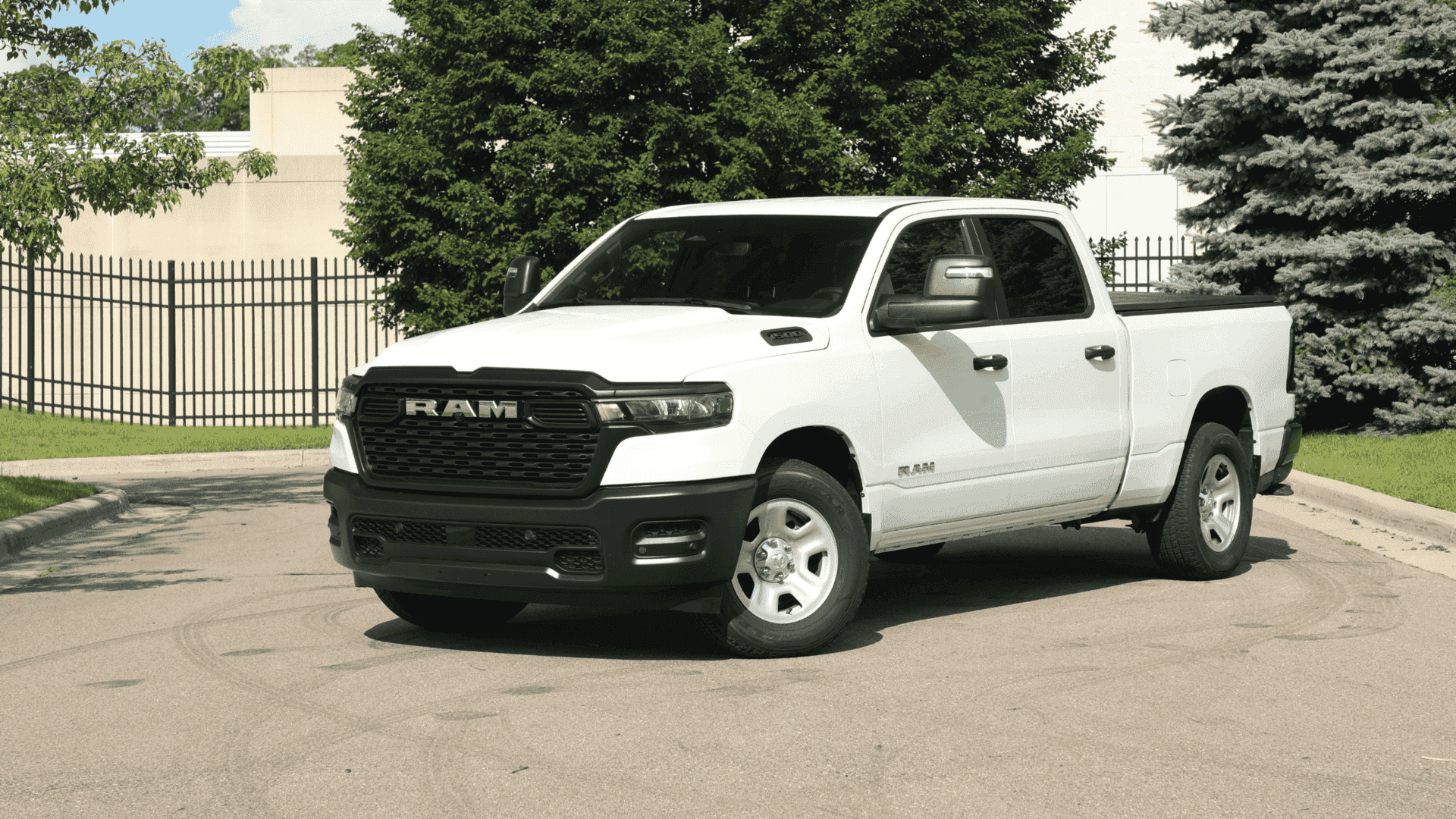 2025 Ram 1500 parked near a fenced area with greenery and urban buildings in the background