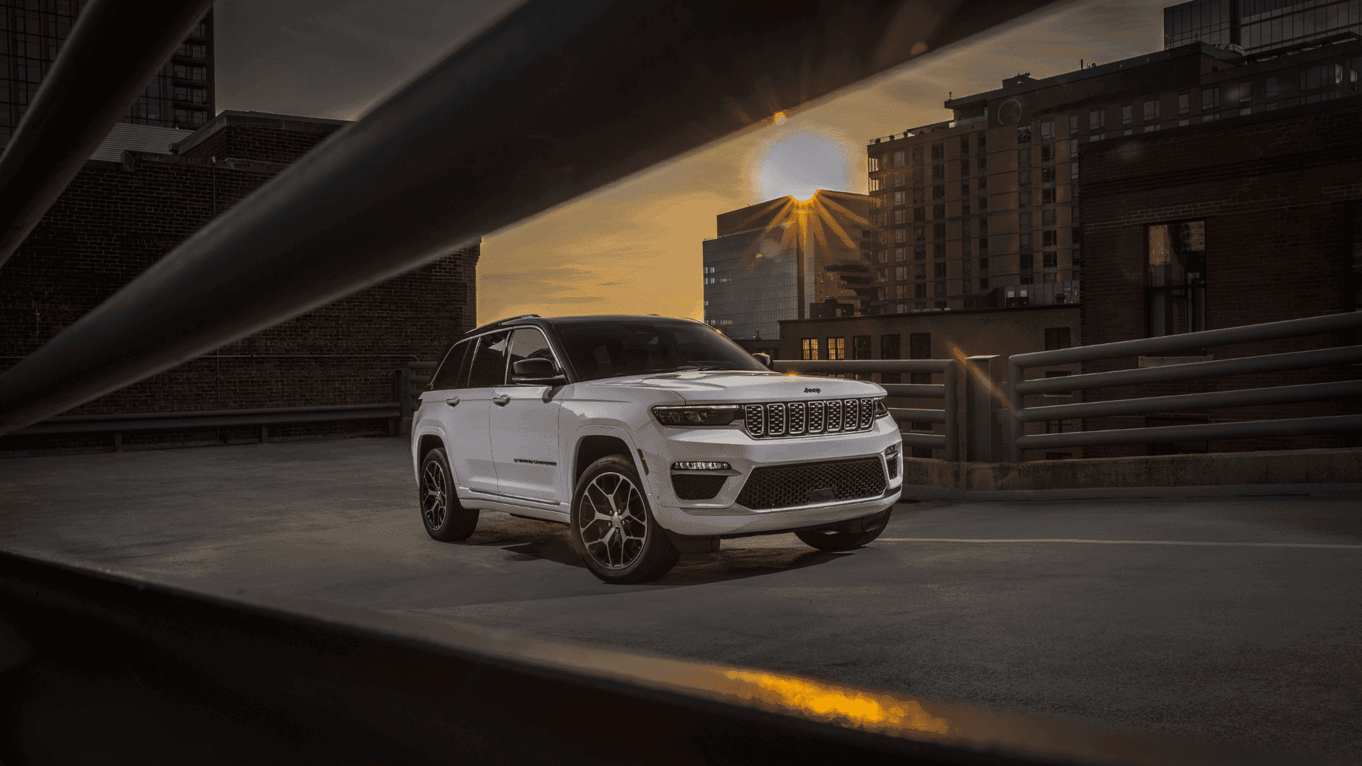 White 2025 Jeep® Grand Cherokee 4xe parked on rooftop at sunset with city skyline view