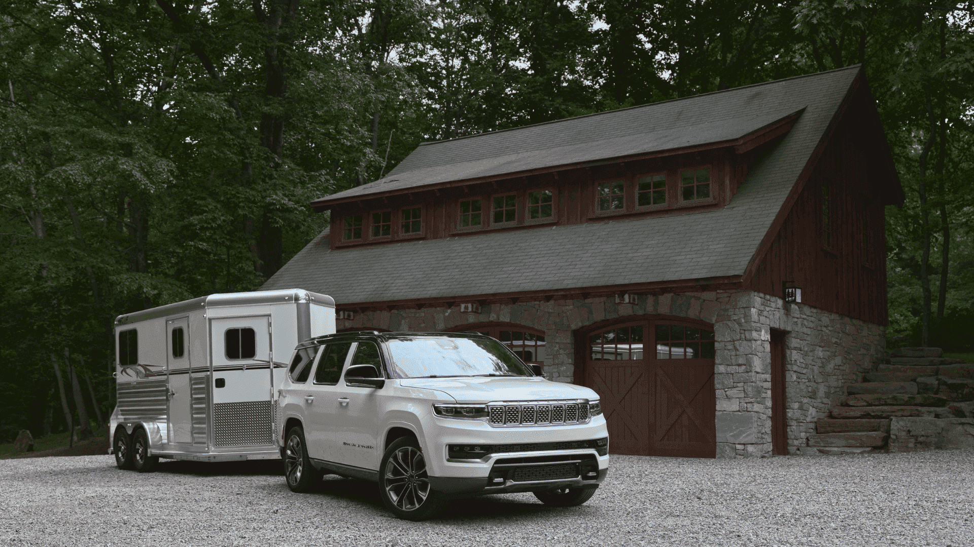 2025 Grand Wagoneer in white towing a horse trailer outside a rustic stone and wood home