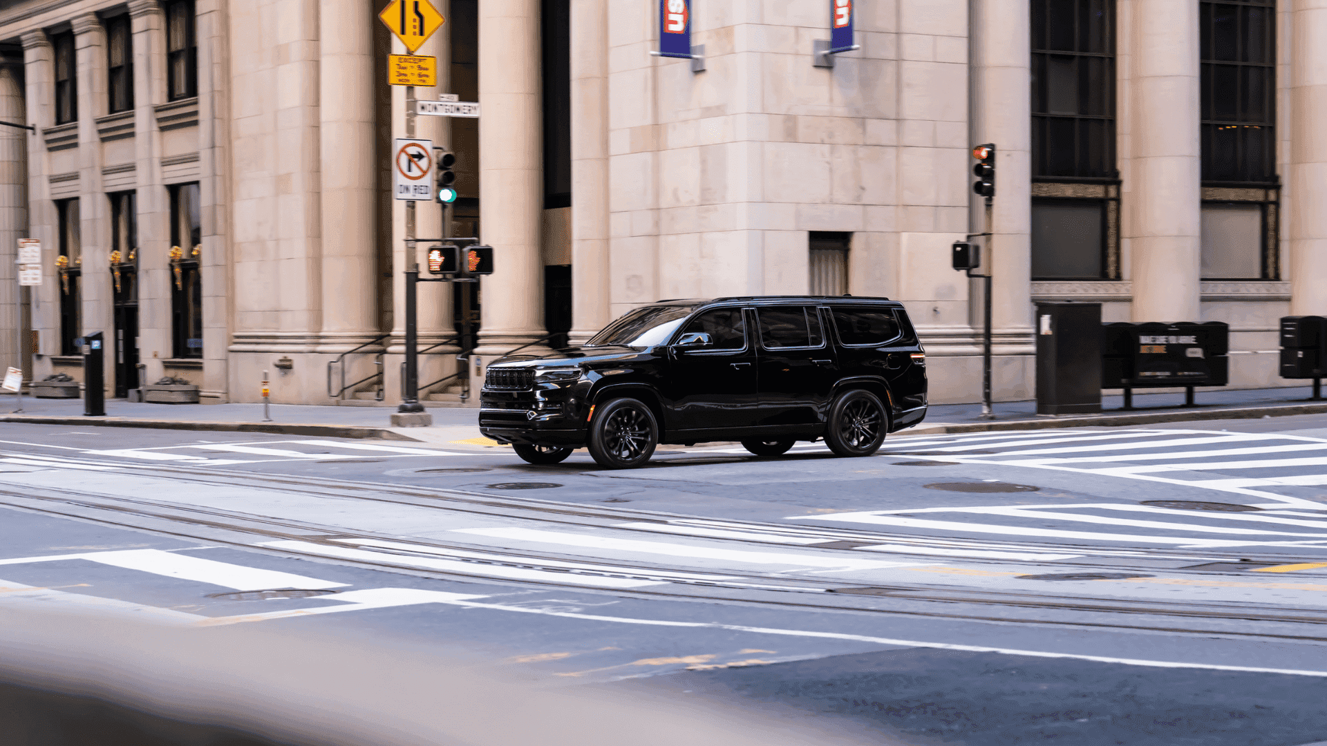 Black 2025 Jeep® Grand Wagoneer turning at downtown intersection with skyscrapers in background