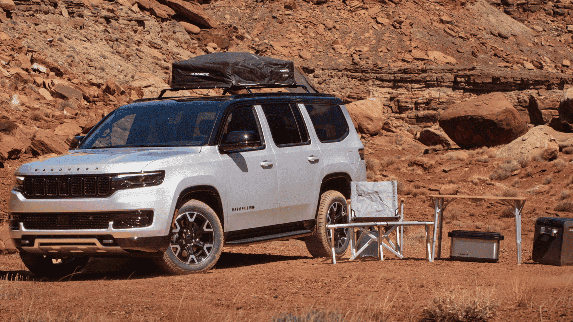 2025 Jeep® Wagoneer in silver parked in red rock desert with rooftop tent, camp chairs, and gear setup