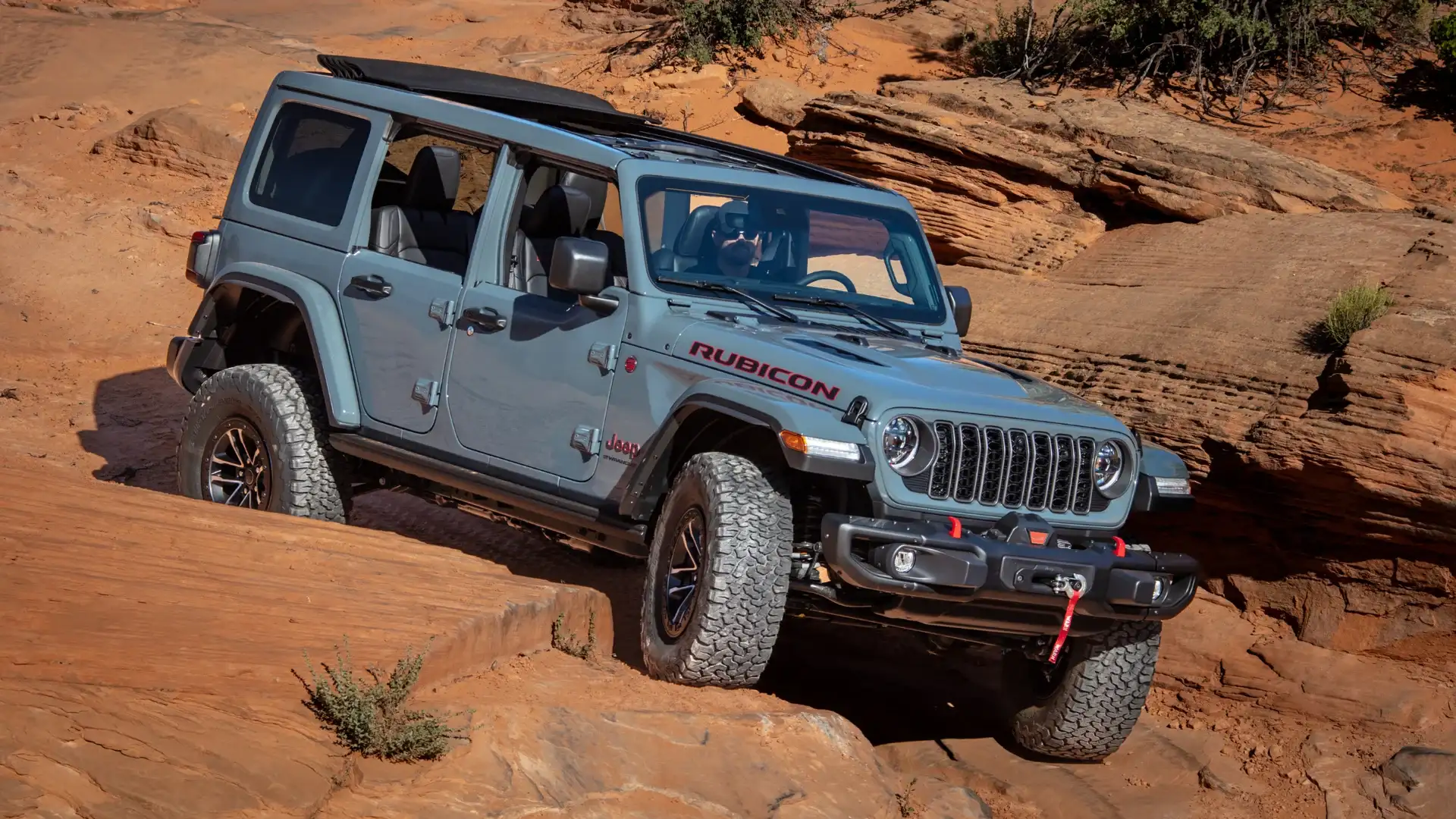 2025 Jeep Wrangler driving off-road trail in rugged mountain desert landscape.