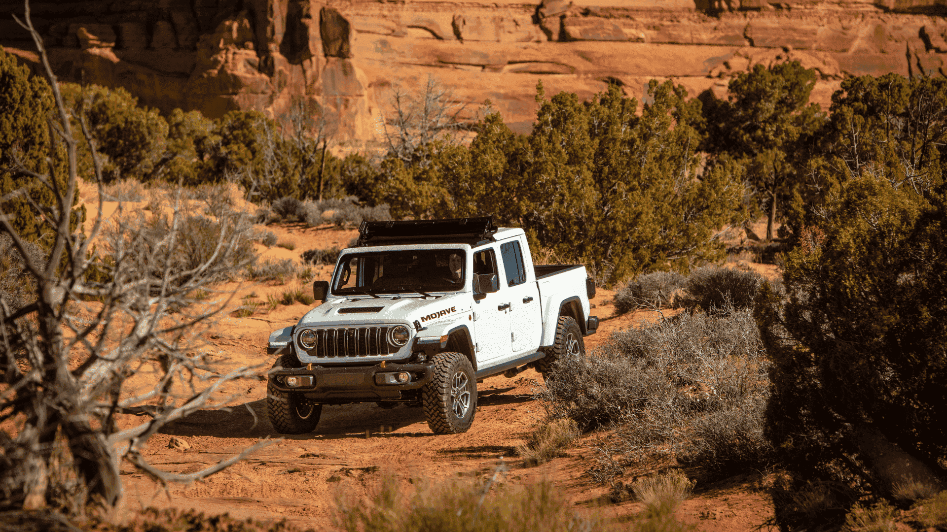 White 2025 Jeep Gladiator Mojave trim navigating a rocky trail in a red rock desert landscape.