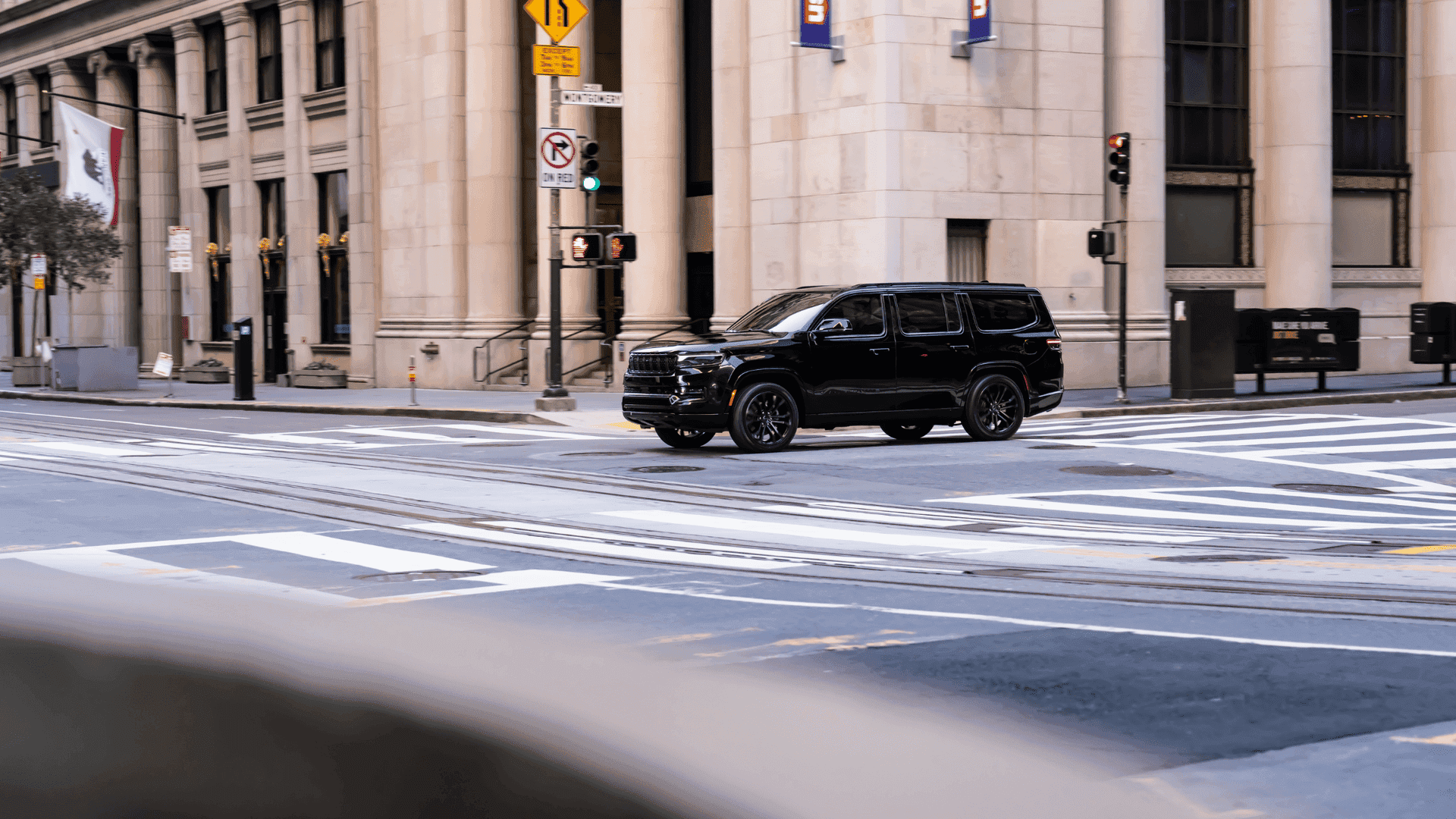 Black 2025 Jeep Grand Wagoneer driving through an empty downtown intersection near classical buildings.