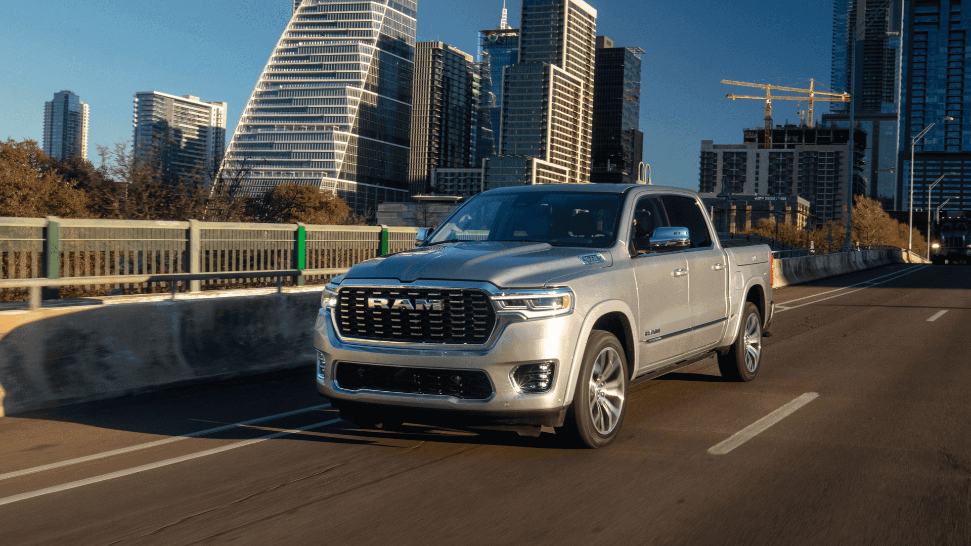 Silver 2025 Ram 1500 driving on an urban bridge with high-rise buildings in the background.