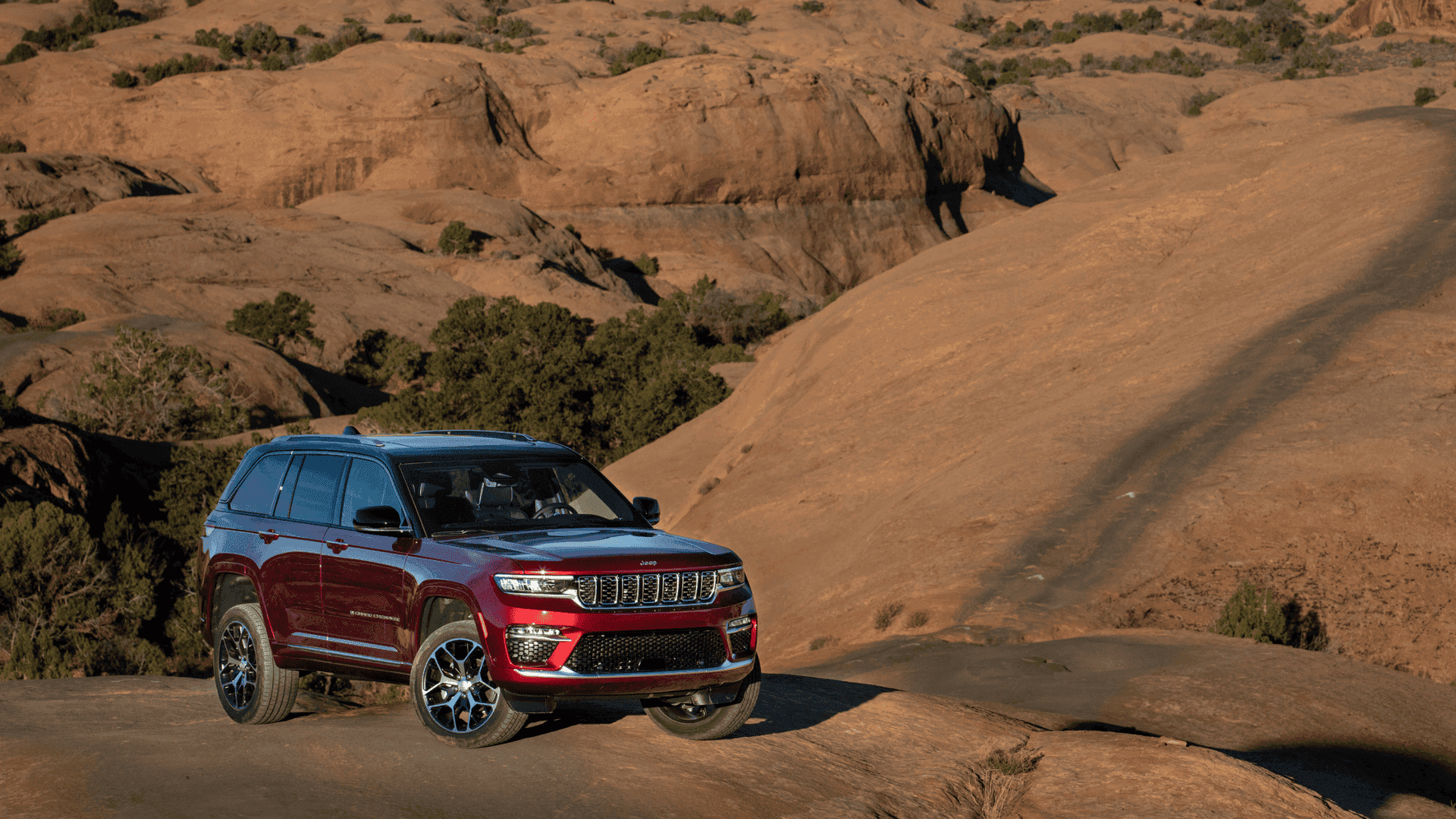 Red 2026 Jeep Grand Cherokee parked on rugged desert terrain near sandstone formations.