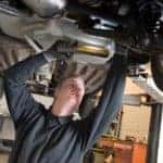 A mechanic is checking the technical state underneath a lifted car on a bridge in a garage.