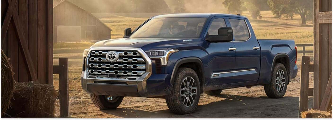 Front three-quarter view of a blue 2026 Toyota Tundra parked by a wooden barn.